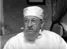 a black and white photo of a man with a beard wearing a surgical cap and gown .