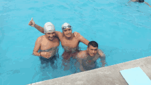 three men are posing for a picture in a swimming pool and one of them is wearing a reebok swim cap