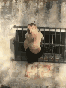 a woman is squatting down in front of a window with bars on it