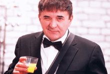 a man in a tuxedo and bow tie holds a glass of orange juice