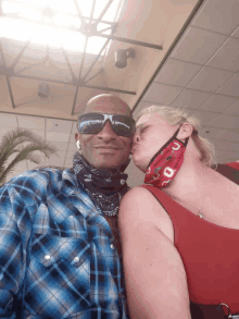 a man wearing sunglasses and a bandana kisses a woman wearing a face mask that says texas