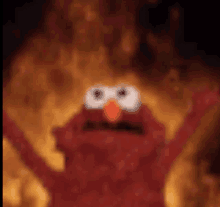 elmo from sesame street is standing in the middle of a fire .