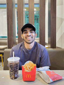 a man sits at a table with a mcdonald 's box of french fries and a soda