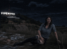 a woman sits in a field with a vinewood sign in the background