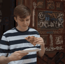 a young man in a striped shirt is eating a slice of pizza in front of a sign that says bon lar