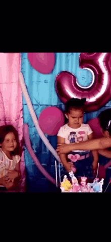 a little girl stands in front of a birthday cake with a pink number 5 balloon in the background