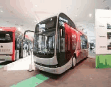 a red and white double decker bus is parked in a room next to a red bus .