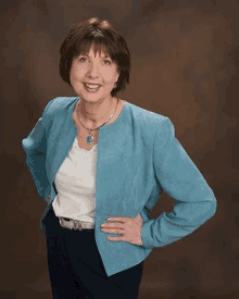 a woman in a blue jacket and white shirt is standing with her hands on her hips and smiling .