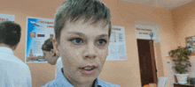 a young boy stands in front of a poster that says " государственный "