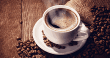 a cup of coffee on a saucer surrounded by coffee beans on a wooden table