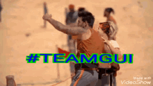 a man and a woman are standing on a sandy beach with the words #teamgui written on the bottom