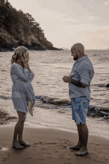 a man and a woman standing on a beach covering their eyes