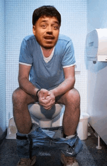 a man in a blue shirt is sitting on a toilet with his pants down