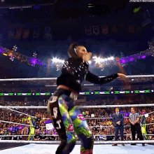 a woman in a colorful outfit is dancing in a wrestling ring while a referee looks on .