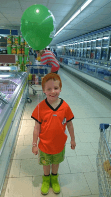 a boy holding a green balloon in a store