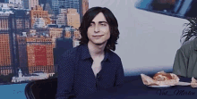 a young man with long hair is sitting at a table with a plate of food in front of him .