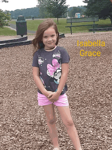 a little girl wearing a minnie mouse shirt and pink shorts is standing in a park