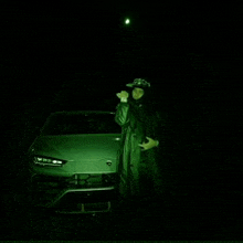 a man in a hood is standing in front of a car in the dark .