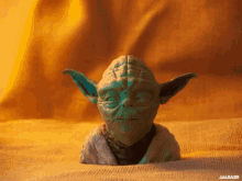 a statue of yoda sits on a table with a yellow background