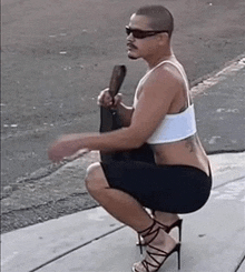 a man squatting down wearing high heels and a tank top