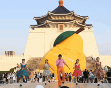 a group of people are dancing in front of a large yellow pear that says jo alone on it