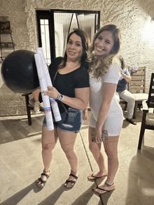 two women standing next to each other holding a black balloon and confetti