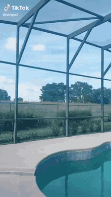 a swimming pool is surrounded by a screened in area with a fence and trees in the background .