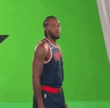 a basketball player is standing in front of a green screen and looking at the camera .