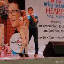 a man and a woman singing on a stage in front of a sign that says the achy break heart mall show