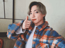 a young man in a plaid jacket gives a thumbs up