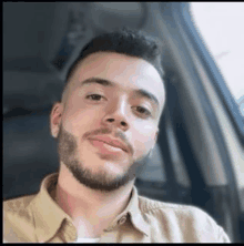 a man with a beard is sitting in a car and smiling .