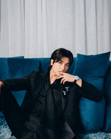 a man in a black suit is sitting on a couch with blue pillows