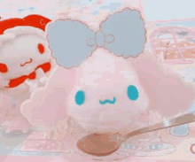 a stuffed animal with a bow on its head is sitting next to a spoon on a table .