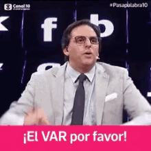 a man in a suit and tie stands in front of a screen that says " el var por favor "