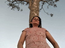 a woman in a pink lace dress is leaning against a tree