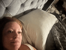 a woman is laying on a bed with a white pillow behind her