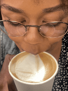 a woman wearing glasses smells a cup of coffee