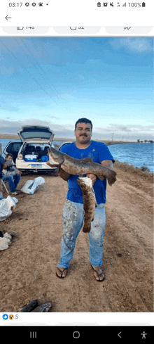 a man is holding a large fish in front of a car