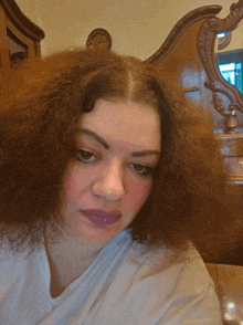 a woman with very curly hair is sitting in front of a wooden dresser