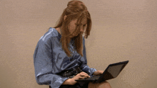 a woman in a blue satin shirt is using a laptop computer