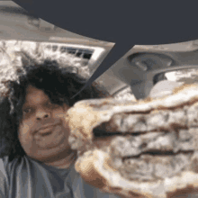 a man with curly hair is holding a hamburger in his hand while sitting in a car .