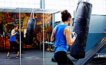 a woman in a blue tank top is boxing in a gym with a fox 6 bench in the background