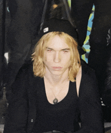 a young man with long blonde hair wearing a black hat with the letter a on it