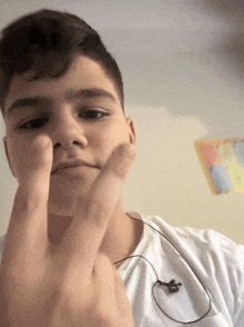 a young man wearing ear buds and a white shirt giving the middle finger