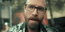 a man with glasses and a beard is wearing a floral jacket