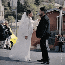 a bride and groom are standing next to each other in front of a group of people and a yellow car