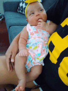 a baby wearing a headband is being held by a man wearing a black and yellow shirt with the number 5 on it