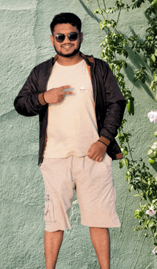 a man wearing sunglasses and a white shirt stands in front of a wall