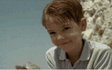 a young boy with red hair and a white shirt is smiling