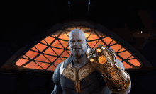 thanos holds up his infinity gauntlet in front of a red window